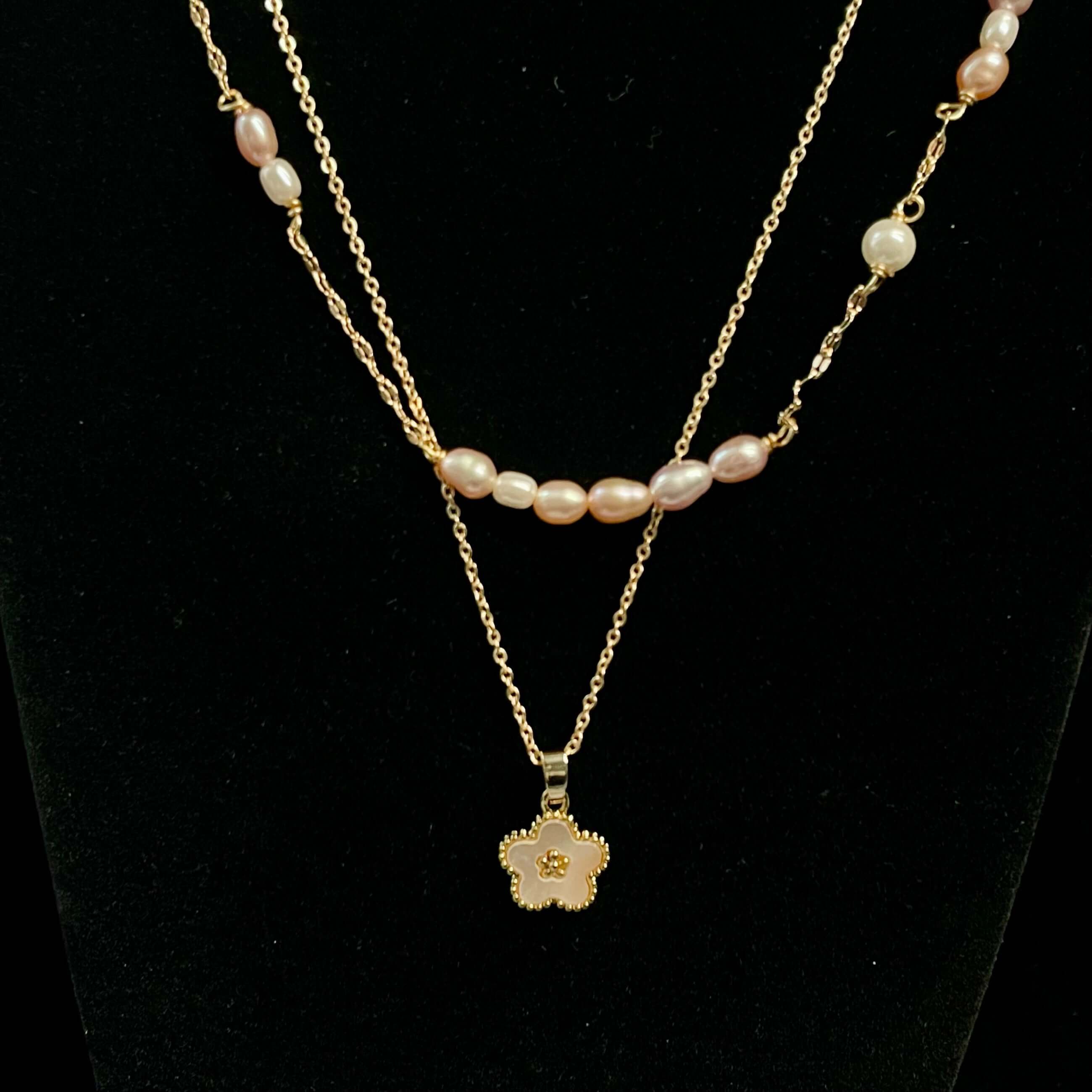 Layered pearl and gold chain necklace with enamel flower pendant displayed against black velvet backdrop
